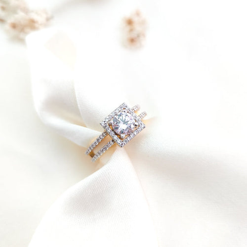 An elegant sterling silver engagement ring with a central white gemstone and smaller diamond simulant stones, presented on a satin fabric.