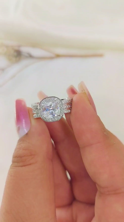 &nbsp;white stone, embraced by a radiant halo setting and supported by a luxurious triple shank band.